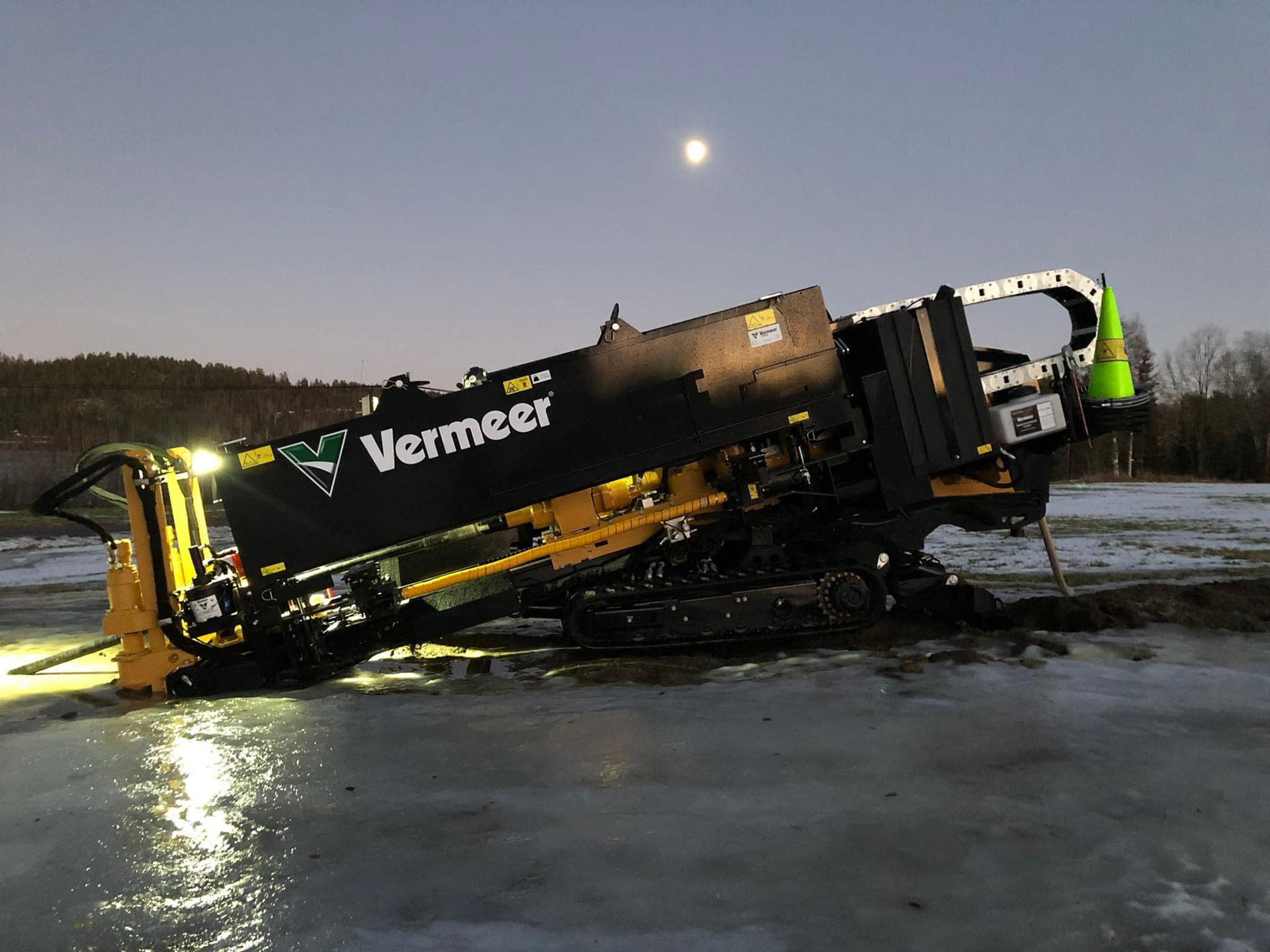 Maszyna Vermeer leży na lodzie w zimowym otoczeniu, z widoczną pełnią księżyca na tle nieba.